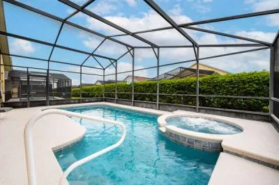 Showing pool and spa with screen enclosure and privacy hedge in the back of the property.