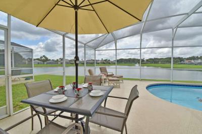 Covered poolside dining table with umbrella overlooking screened pool and lake view.