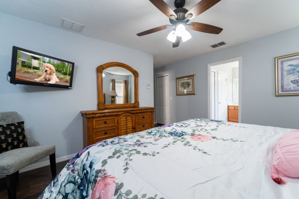 Master bedroom featuring a king bed, dresser with mirror, wall mounted TV, and ceiling fan.