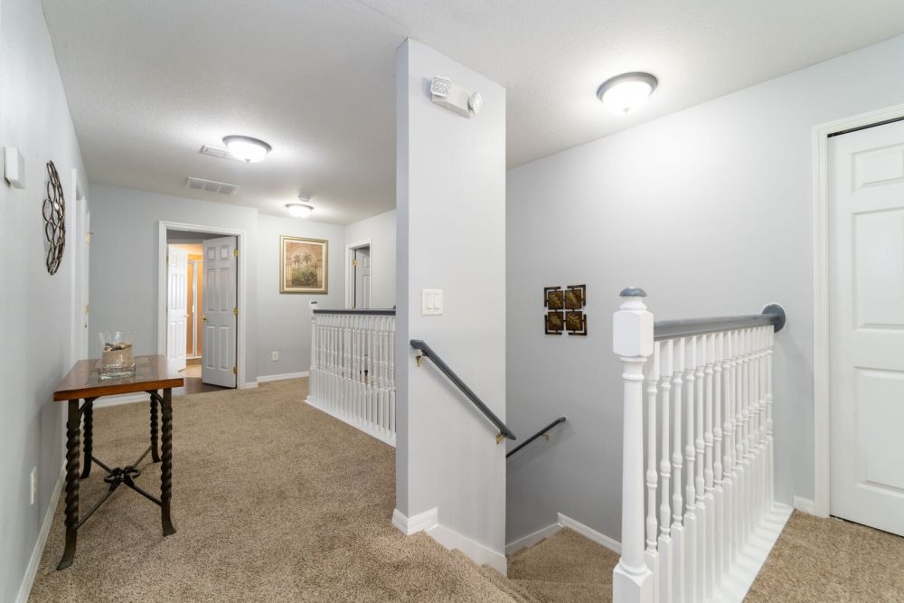 Upstairs hallway with carpeted floors, stair railing, and access to multiple bedrooms.