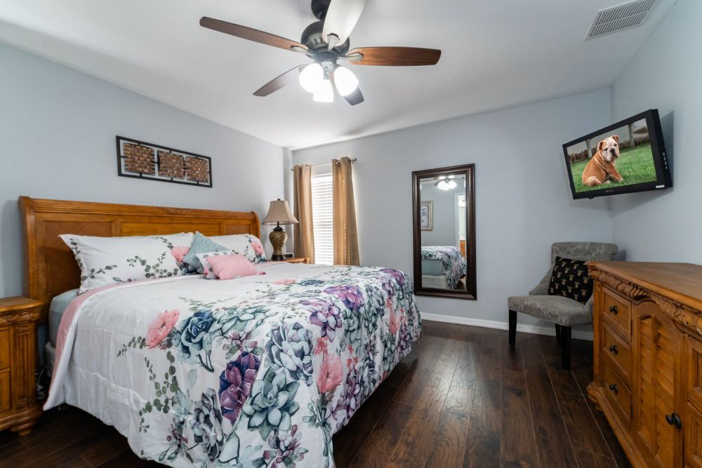 Upstairs master bedroom with king bed, hardwood flooring, ceiling fan, and wall mounted TV.