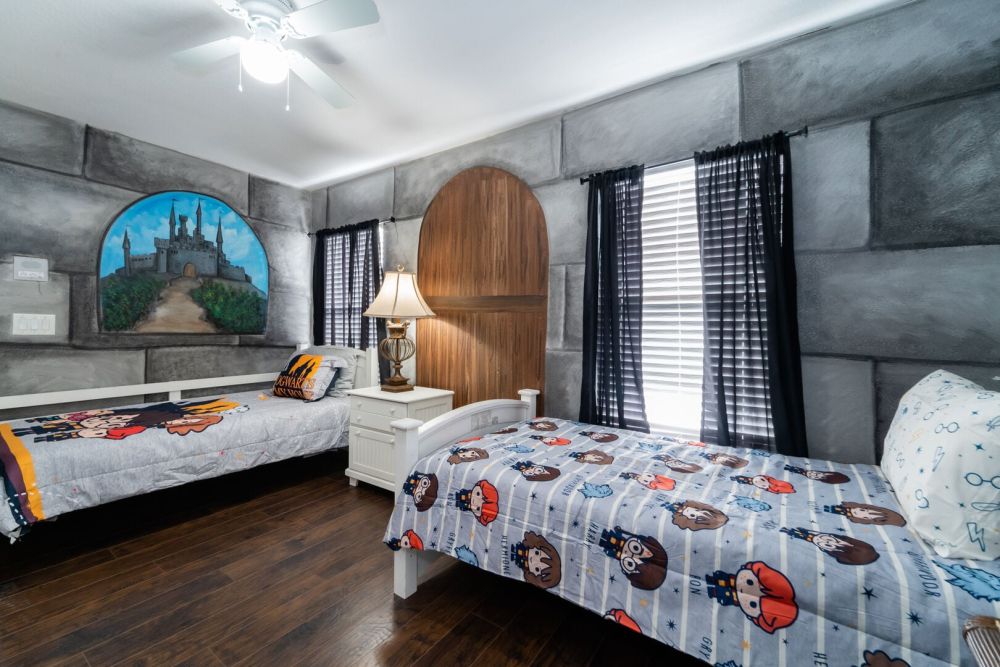 Themed kids bedroom with two twin beds, decorative wall murals, ceiling fan, and hardwood flooring.