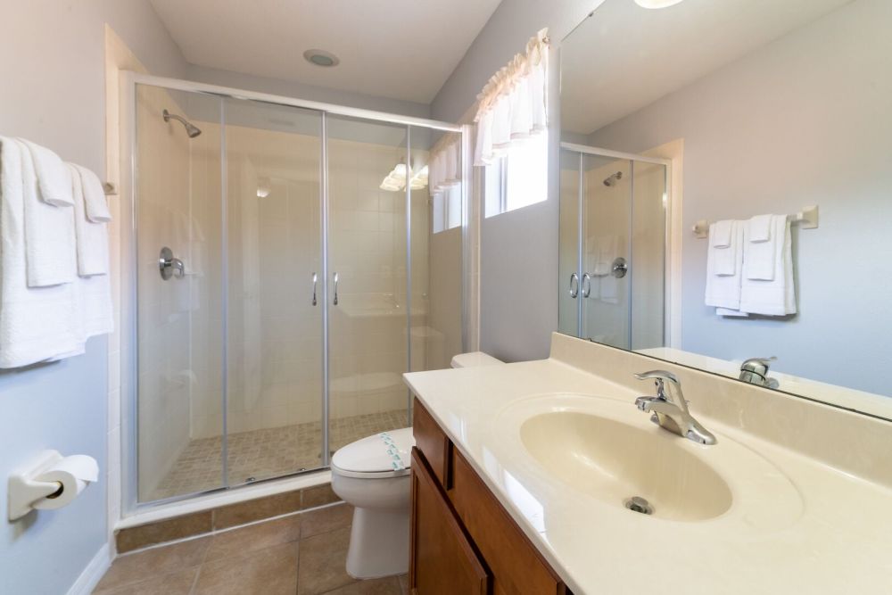 En-suite bathroom with single sink vanity, glass enclosed shower, and tile flooring.