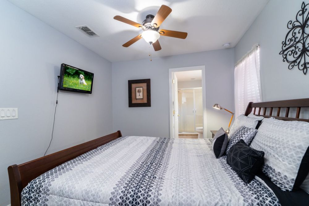 Upstairs bedroom with queen bed, ceiling fan, wall mounted TV, and en-suite bathroom access.