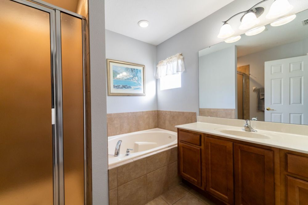 Upstairs en-suite bathroom with soaking tub, glass enclosed shower, and vanity with mirror.