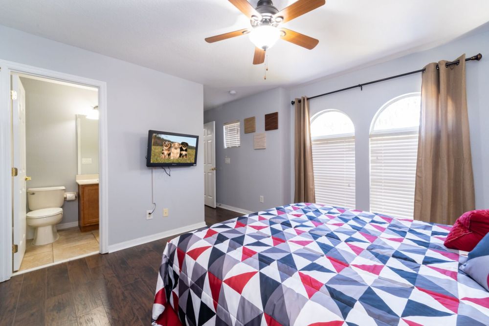 Upstairs bedroom with ceiling fan, wall mounted TV, and en-suite bathroom access.