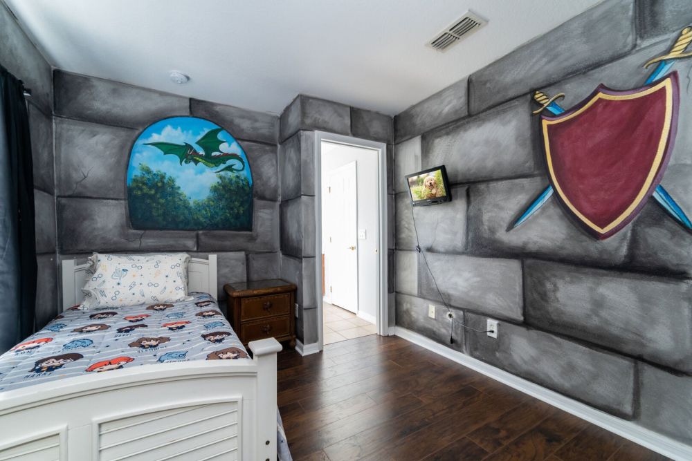 Themed kids bedroom with twin bed, decorative wall murals, hardwood flooring, and wall mounted TV.