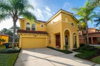 Two story vacation home with palm trees, private driveway, and covered entryway in a quiet residential setting.