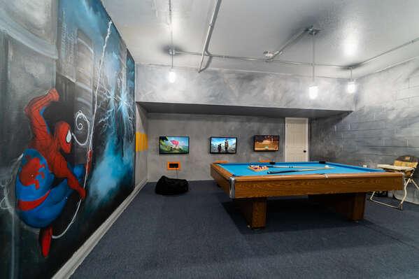Spacious indoor game room with a pool table, wall mounted TVs, and large superhero themed wall mural.