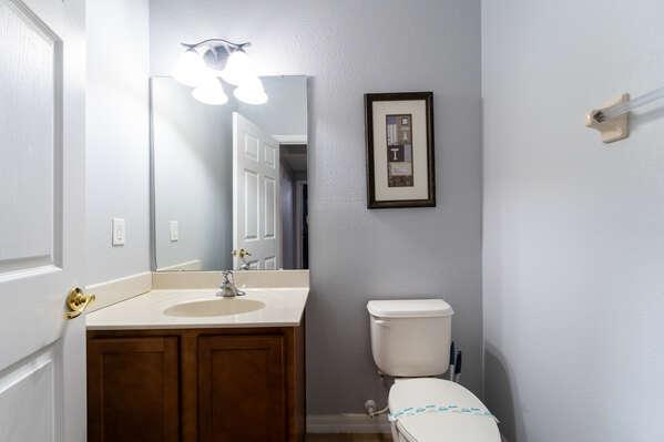 Downstairs shared bathroom featuring a single sink vanity, mirror, and toilet.