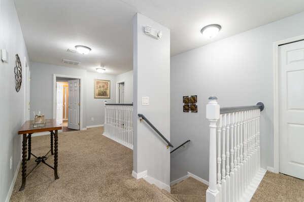 Upstairs hallway with carpeted floors, stair railing, and access to multiple bedrooms.