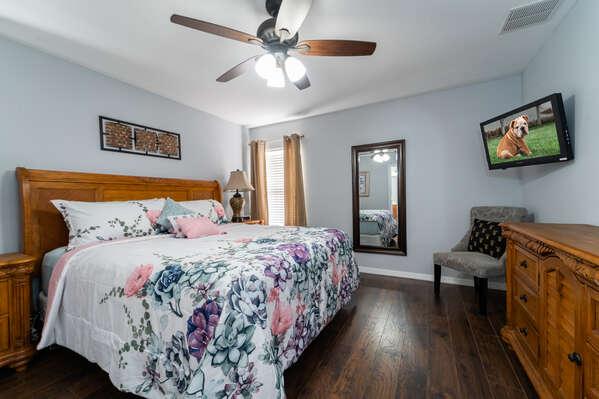 Upstairs master bedroom with king bed, hardwood flooring, ceiling fan, and wall mounted TV.