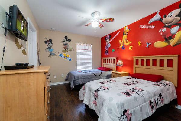 Upstairs themed kids bedroom with two twin beds, colorful wall murals, ceiling fan, dresser, and wall mounted TV.