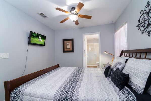 Upstairs bedroom with queen bed, ceiling fan, wall mounted TV, and en-suite bathroom access.