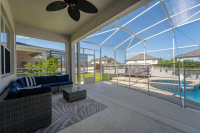 Covered lanai seating with screened in pool view, ceiling fan, and safety fence.