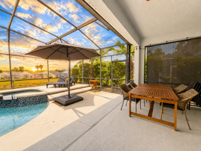 Pool area with sunset view showing outdoor dining table seating for 4 and an umbrella.
